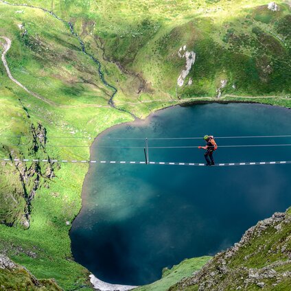 Ein Kletterer auf einer Seilbrücke oberhalb eines Bergsees in der Silvretta Montafon. | © Silvretta Montafon - Bertram Waldner