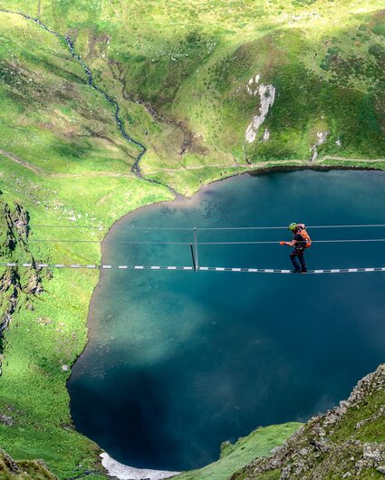 Ein Kletterer auf einer Seilbrücke oberhalb eines Bergsees in der Silvretta Montafon. | © Silvretta Montafon - Bertram Waldner