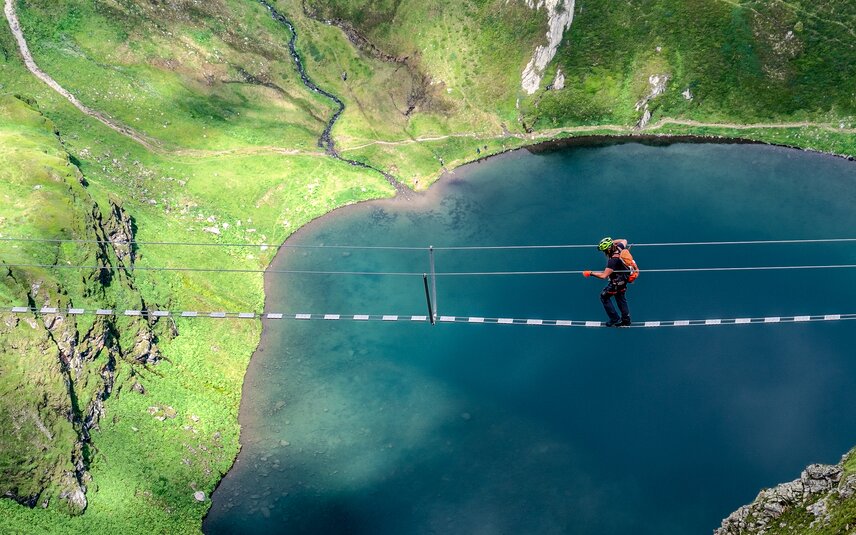 Ein Kletterer auf einer Seilbrücke oberhalb eines Bergsees in der Silvretta Montafon. | © Silvretta Montafon - Bertram Waldner
