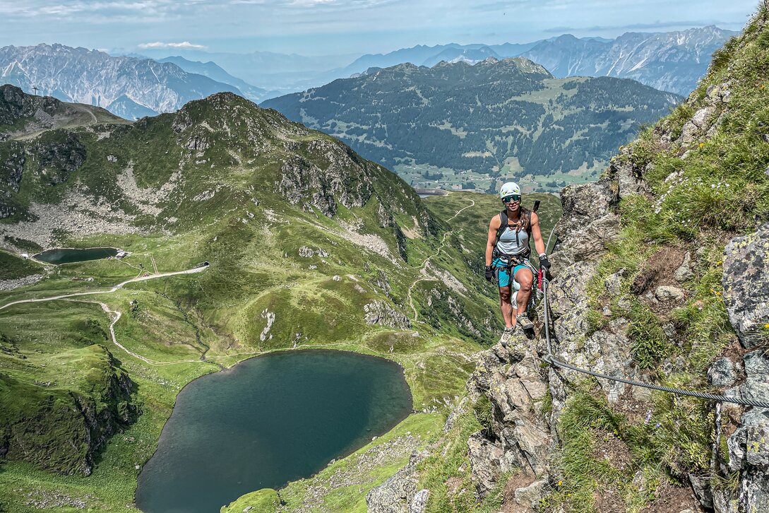 Eine Kletterin steht am Seil im Klettersteig mit Blick ins Seetal am Hochjoch in der Silvretta Montafon. | © Silvretta Montafon - Vanessa Strauch