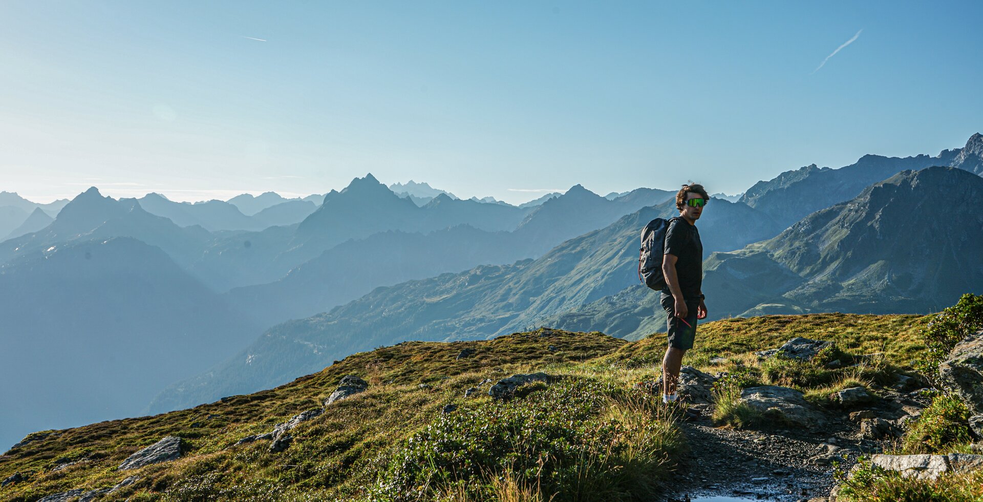 Ein Mann wandert in den Bergen im Sommer mit Aussicht auf die umliegenden Gipfel. | © Silvretta Montafon - Vanessa Strauch