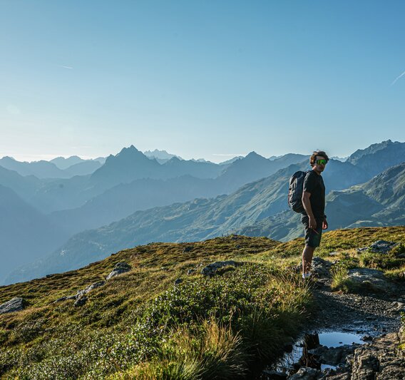 Ein Mann wandert in den Bergen im Sommer mit Aussicht auf die umliegenden Gipfel. | © Silvretta Montafon - Vanessa Strauch