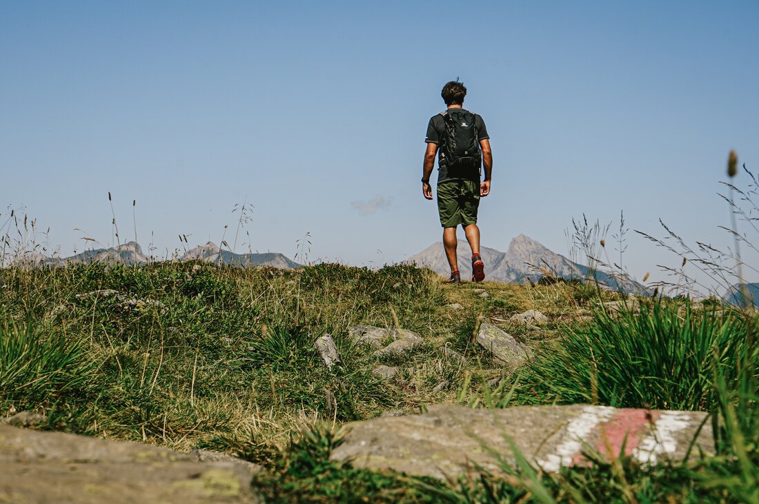 Ein Mann in kurzen Hosen und schwarzem Rpucksack läuft auf einem Wanderweg in den Bergen im Sommer. | © Vanessa Strauch - Silvretta Montafon