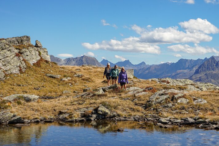 Drei junge Frauen wandern im herbstlichem Gebirge zu einem Bergsee. | © Silvretta Montafon - Vanessa Strauch