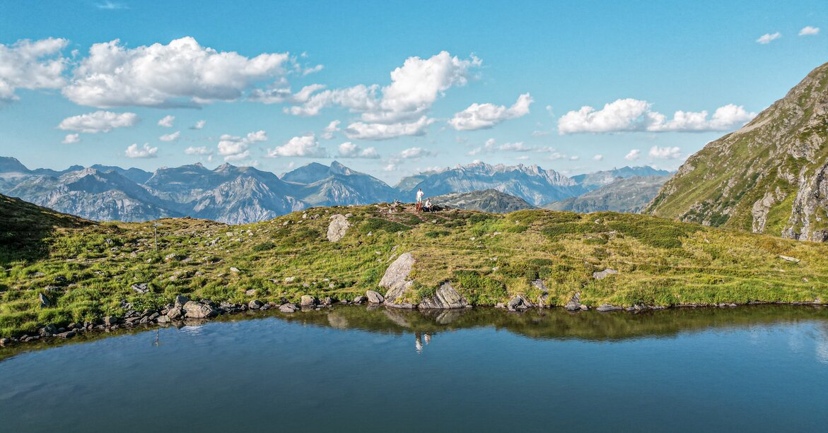Ein Bergsee im Sommer mit zwei Personen in Hintergrund. | © Silvretta Montafon - Vanessa Strauch