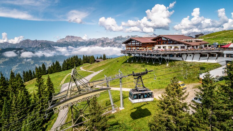Das Kapellrestaurant mit Bergen im Hintergrund und der Hochjoch Bahn im Vordergrund im Sommer | © Silvretta Montafon - Stefan Kothner