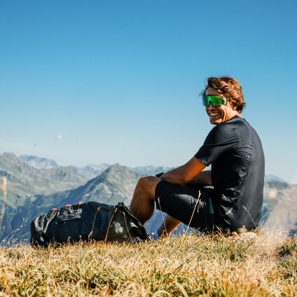 Ein junger Mann mit schwarzer Wanderkleidung und Sonnenbrille genießt die Aussicht auf die Montafoner Bergwelt in der Silvretta Montafon | © Silvretta Montafon - Vanessa Strauch