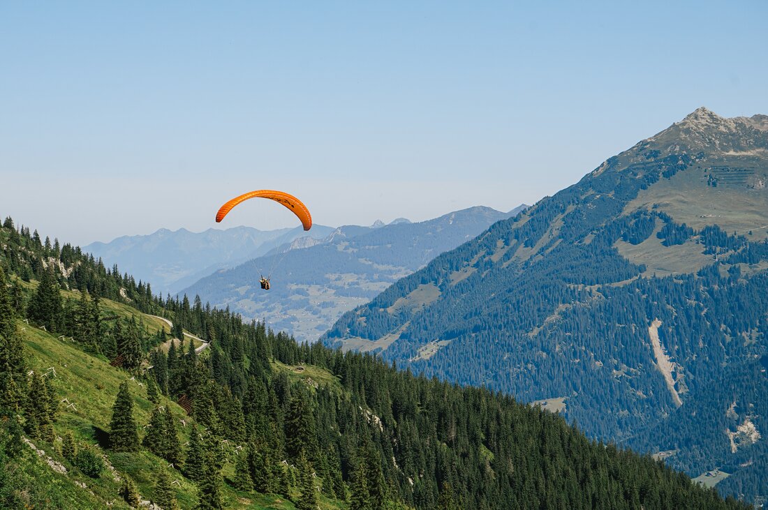 Ein Paraglider fliegt über die Berge eentlang des Wanderweges Lifinar in der Silvretta Montafon. | © Silvretta Montafon - Vanessa Strauch