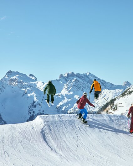 Eine Gruppe von drei Skifahrern und ein Snowboarder springen über eine hohe Schanze auf der Piste im Race Cross in der Silvretta Montafon. | © Silvretta Montafon - Stefan Kothner