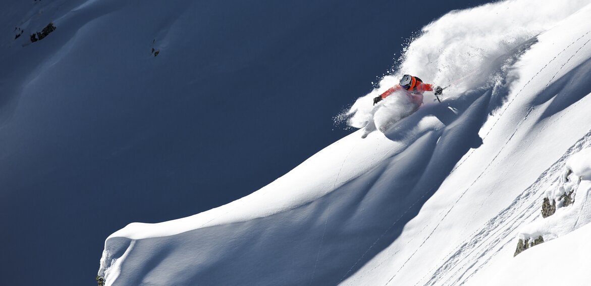 Eine Freerider in orangener Skijacke fährt im Tiefschnee in der Silvretta Montafon. | © Silvretta Montafon - Stefan Kothner