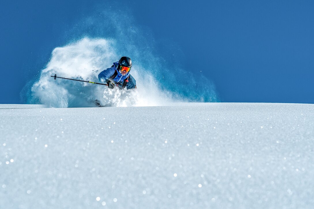 Ein Freerider fährt bei strahlend blauem Himmel im Tiefschnee in der Silvretta MOntafon. | © Silvretta Montafon - Highland Production