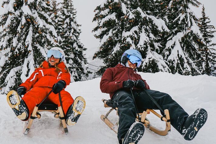 Zwei Freunde lachen beim Rodeln auf der Naturrodelbahn Kapell in der Silvretta Montafon | © Silvretta Montafon - Vanessa Strauch