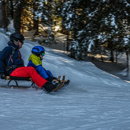 Ein Vater hat Spaß beim Schlittenfahren mit seinem Kind auf der Naturrodelbahn Kapell in der Silvretta Montafon | © Silvretta Montafon - Vanessa Strauch