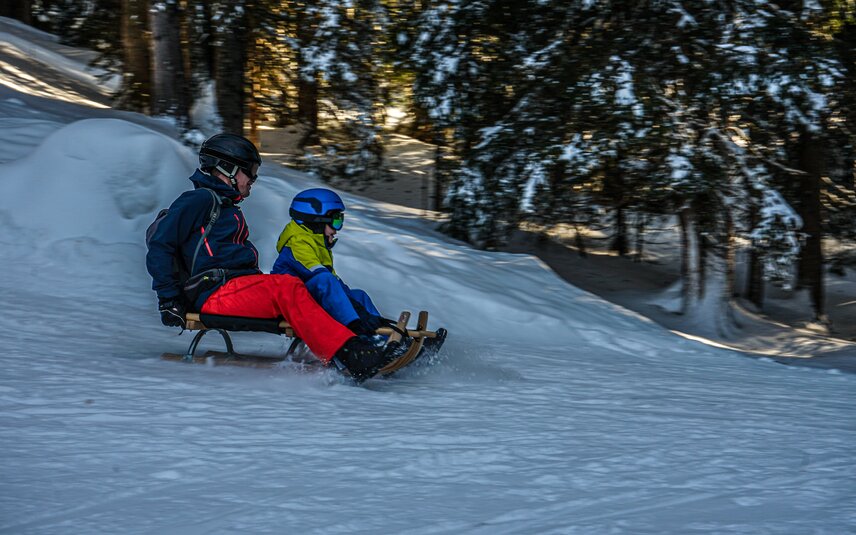 Ein Vater hat Spaß beim Schlittenfahren mit seinem Kind auf der Naturrodelbahn Kapell in der Silvretta Montafon | © Silvretta Montafon - Vanessa Strauch