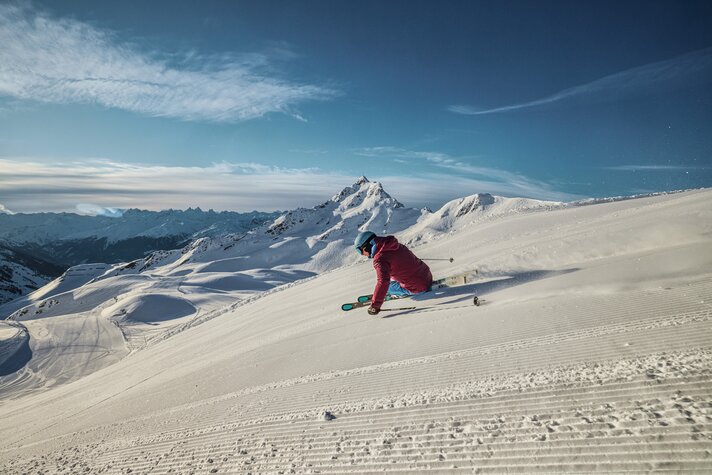 Ein Skifahrer fährt am Morgen über die frisch präparierte Piste mit der Zamangspitze im Hintergrund. | © Silvretta Montafon - Stefan Kothner