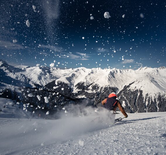 Ein Skifahrer auf der Piste und spritzender Schnee im Vordergrund. | © Silvretta Montafon - Daniel Hug