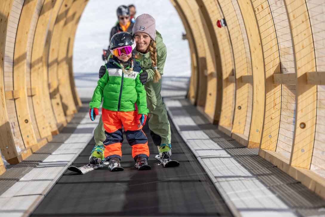 Eine Mutter steht mit ihrer Tochter auf dem überdachten Förderband an der Valisera Bahn Bergstation in der Silvretta Montafon. | © Silvretta Montafon - Torsten Wenzler