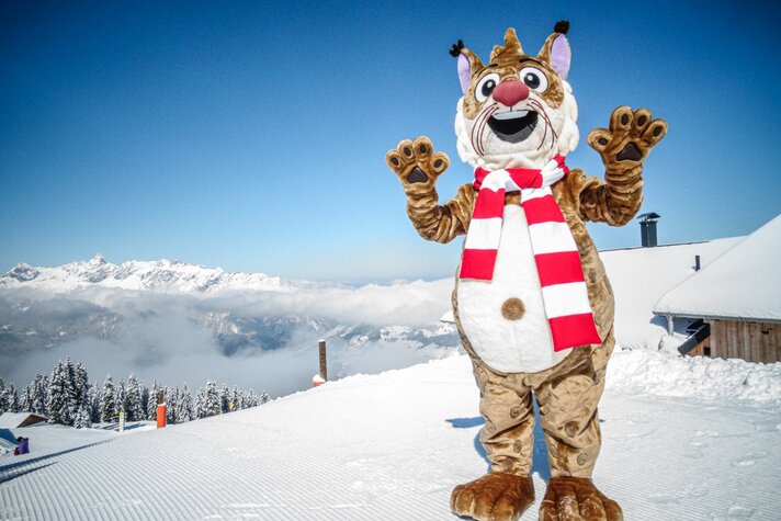 Das Maskottchen Monti Lux steht am Berg im Schnee und winkt in die Kamera. | © Silvretta Montafon