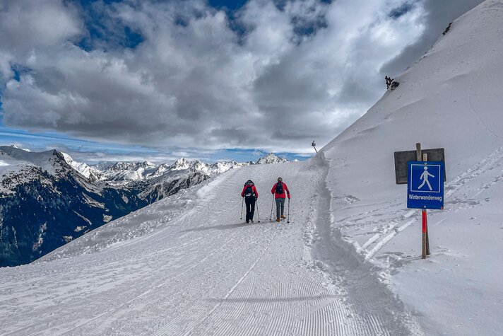 Zwei Personen auf einem verschneiten Winterwanderweg mit Wegweiser im Vordergrund in den Bergen der Silvretta Montafon. | © Silvretta Montafon - Vanessa Strauch