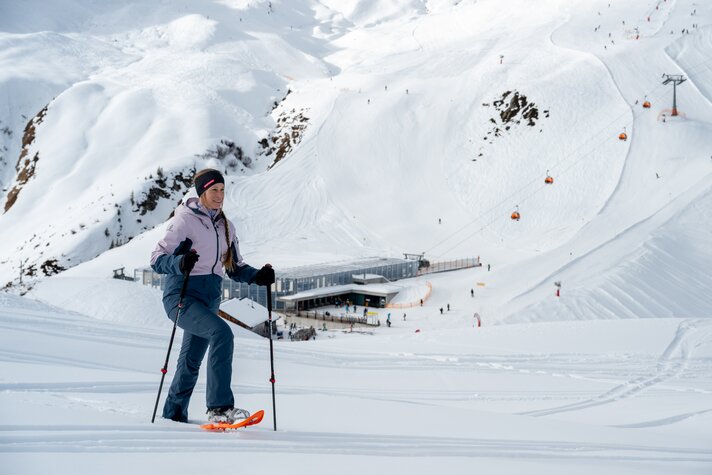 Eine Frau mit Schneeschuhen läuft auf einem Scheeschuhwanderweg in verschneiter Natur hoch oben am Berg. | © Montafon Tourismus - Andreas Marent