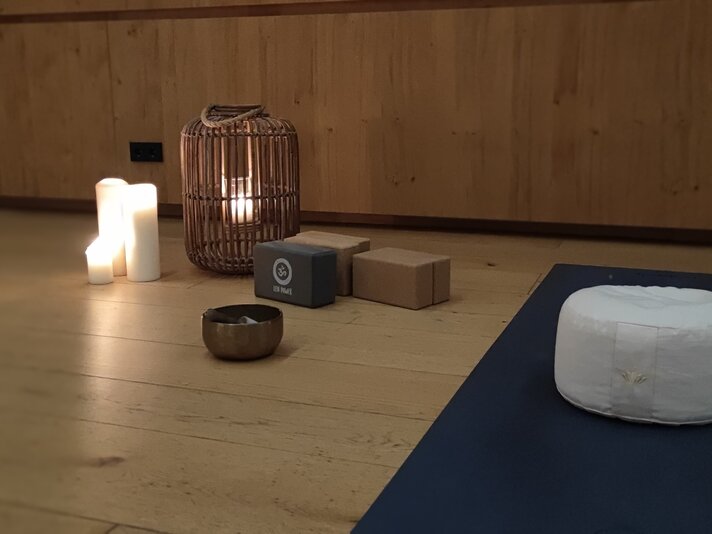 Ein Yogapolster mit einer Kerze und einer Yogamatte in gemütlicher Stimmung | © Tina Fehrenbach - Silvretta Montafon