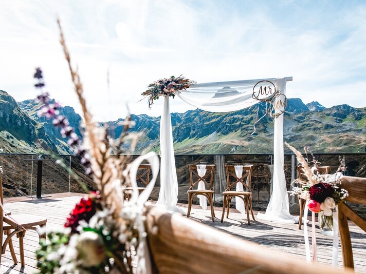 Dekorierter Traubogen und Bestuhlung für eine Hochzeit auf der Terrasse der VINNOVA mit Berge im Hintergrund | © Silvretta Montafon - Patrick Säly