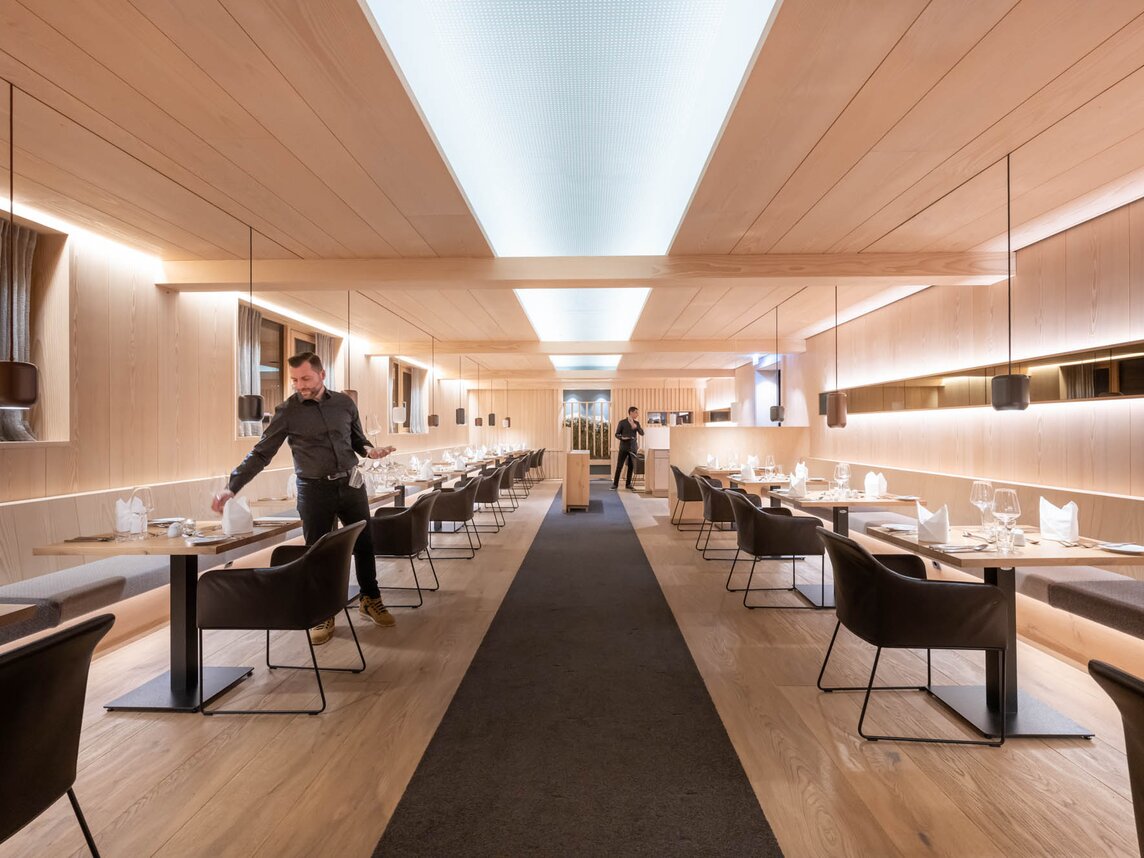 Zwei Kellner decken die Tische im Restaurant mit gemütlichen anthrazitfarbenen Sesseln und Holzambiente | © Silvretta Montafon - blateral