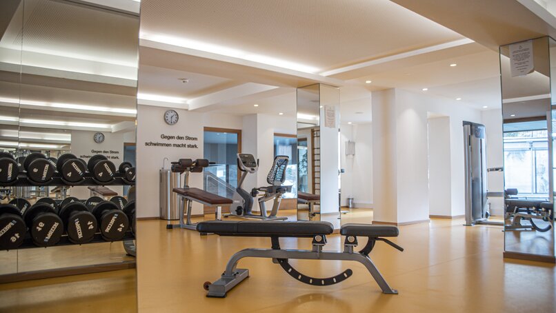 Ein Fitnessraum mit Trainingsgeräten und Hanteln mit gelbem Boden und Spiegeln | © Silvretta Montafon - Mara Baues