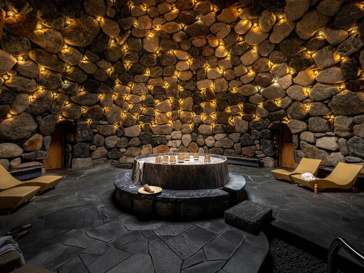 Das Tepidarium mit goldenem Licht an den Steinwänden und gemütlichen Liegen rundum | © Silvretta Montafon - blateral