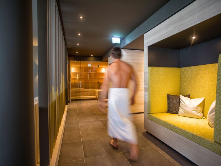 Ein Mann mit einem weißen Handtuch umwickelt läuft durch den Ruhebereich im Spa vom Sporthotel Chalet  | © Silvretta Montafon - blateral