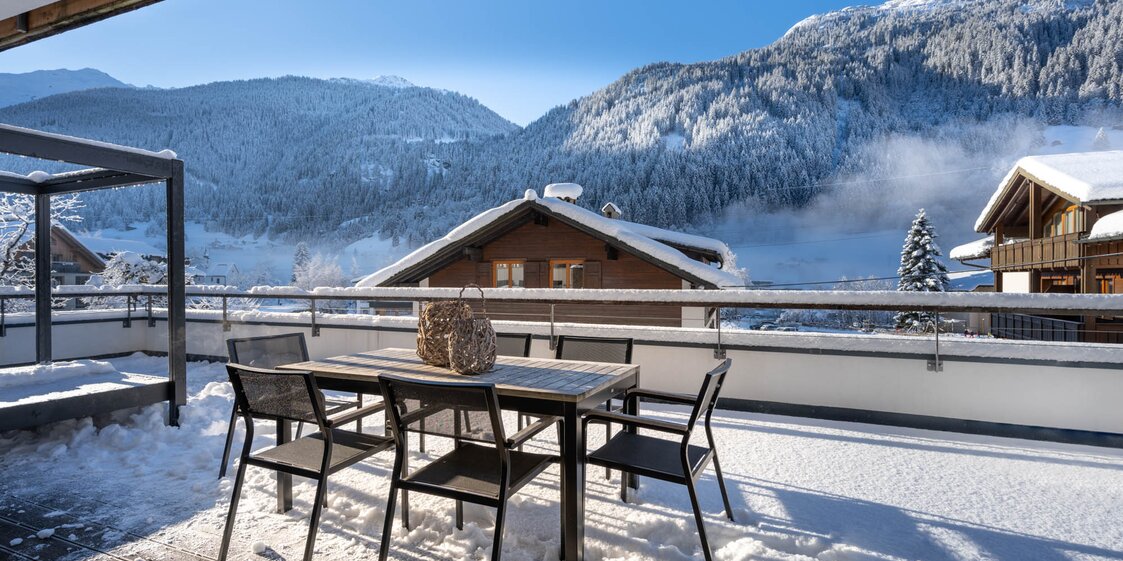 Ein Tisch mit Stühlen auf der verschneiten Terrasse mit einem Ausblick auf die schneebedeckten Berge | © Silvretta Montafon - blateral
