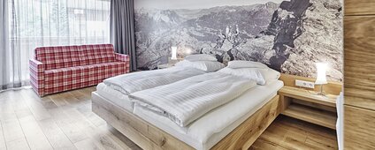 Gemütliche Junior Suite mit Doppelbett und kariertem Sofa | © Silvretta Montafon - Markus Gmeiner
