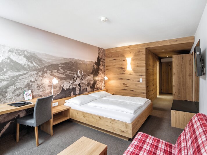 Doppelbett mit großem Schreibtisch und riesigem Wandposter | © Silvretta Montafon - Markus Gmeiner